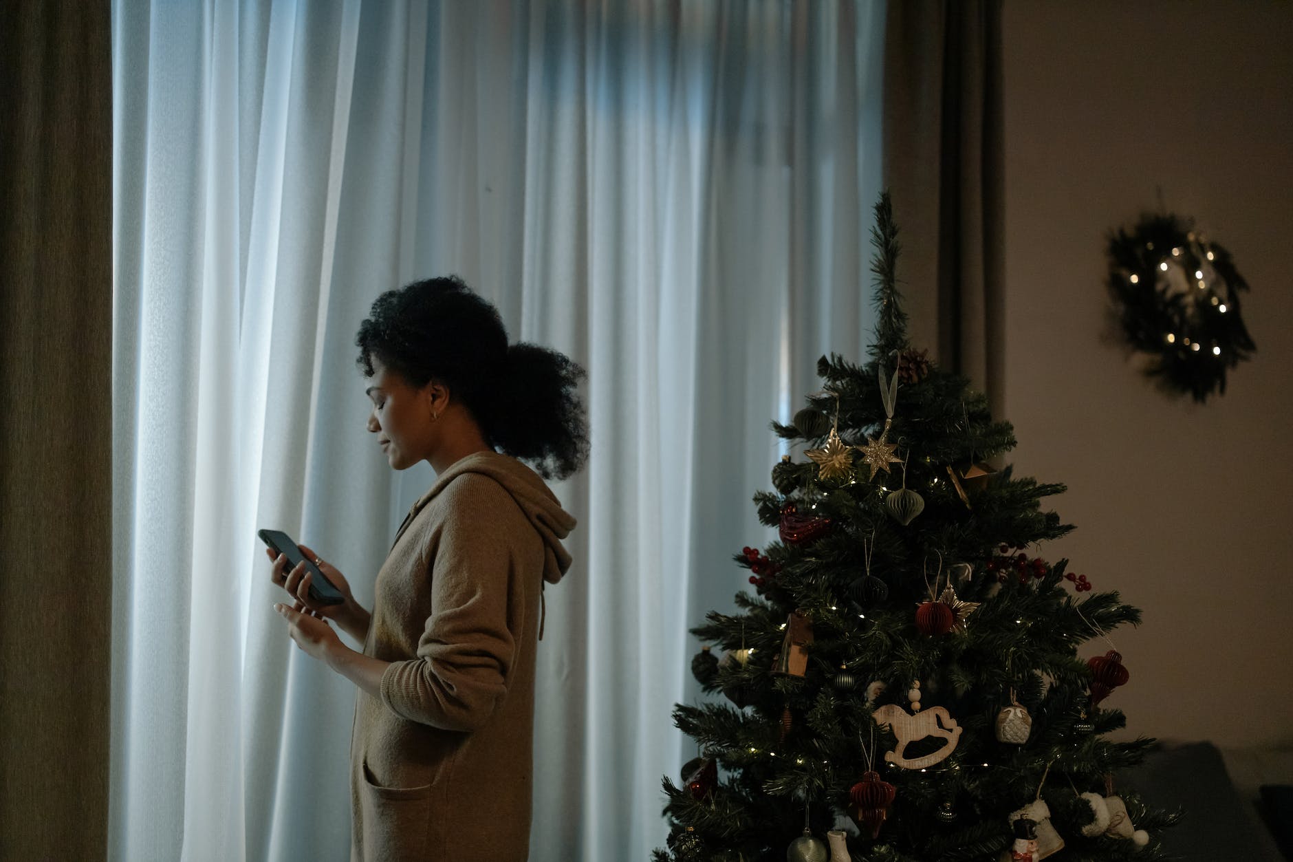 woman with a cellphone standing beside a christmas tree